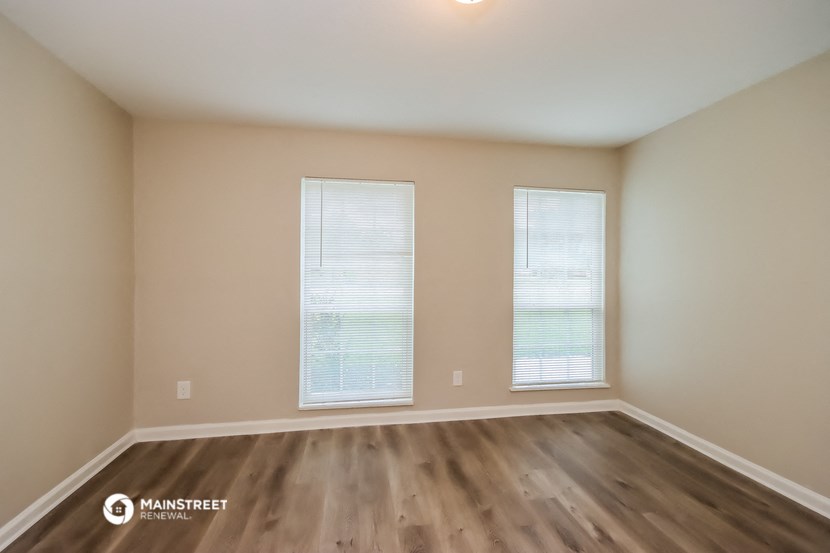 an empty room with wooden floors and two windows