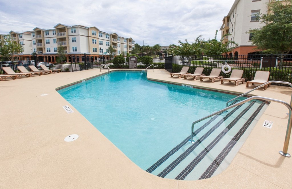a resort style pool with lounge chairs and a building in the background