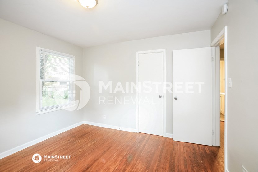 a bedroom with white walls and wood floors and a closet