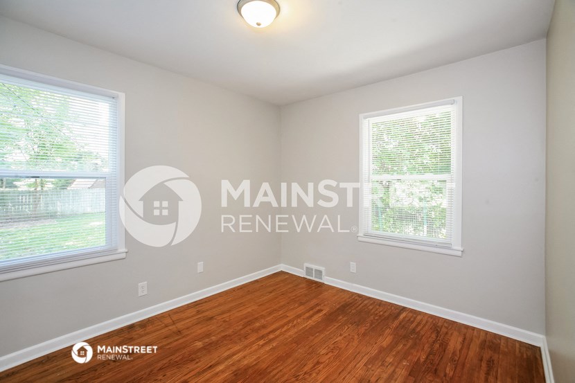 a bedroom with a hard wood floor and two windows