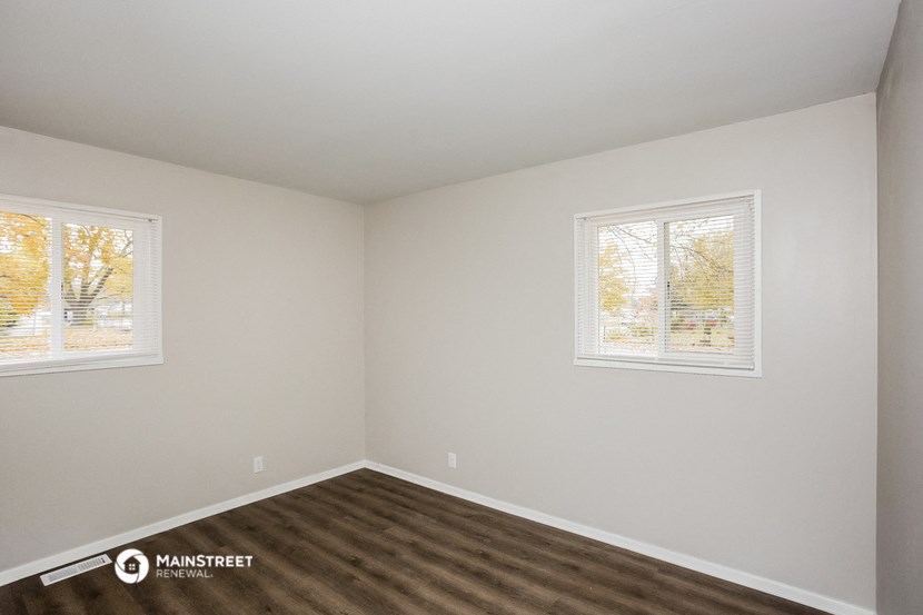 the interior of a small white room with wood flooring and two windows