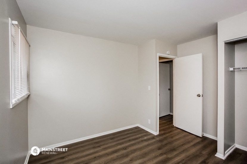 a bedroom with white walls and wood flooring and a closet