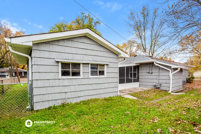 a small gray house with a yard and a chain link fence