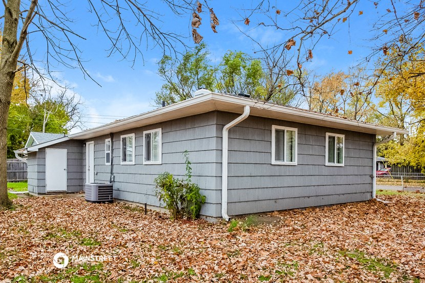 a small gray house in the fall with leaves on the ground