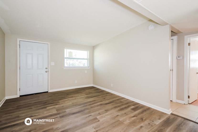 the spacious living room with wood flooring and a white door
