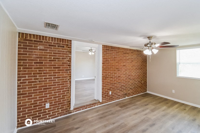 an empty living room with a brick wall and a ceiling fan