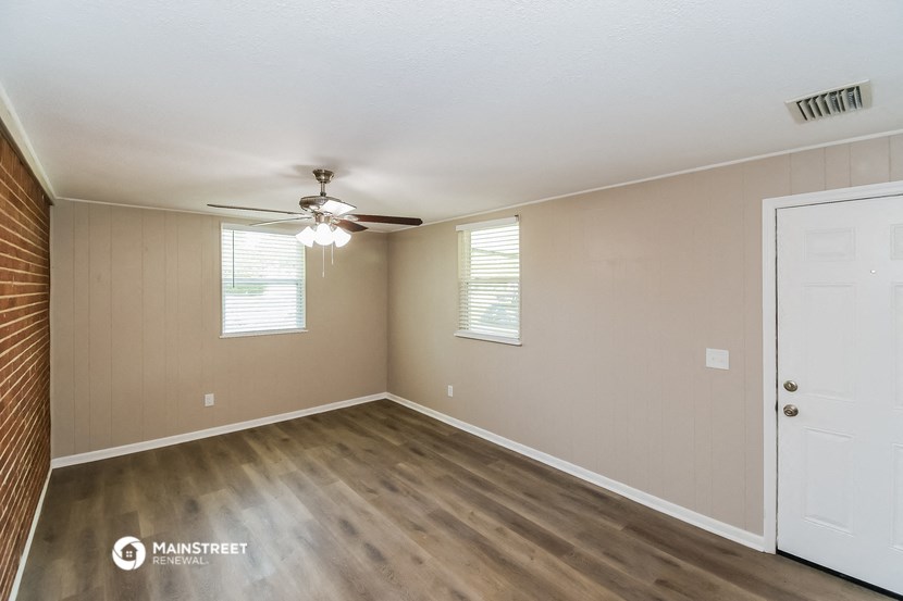 the spacious living room with wood flooring and a ceiling fan