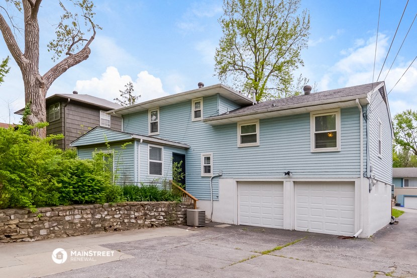 a blue house with a white garage with a stone wall