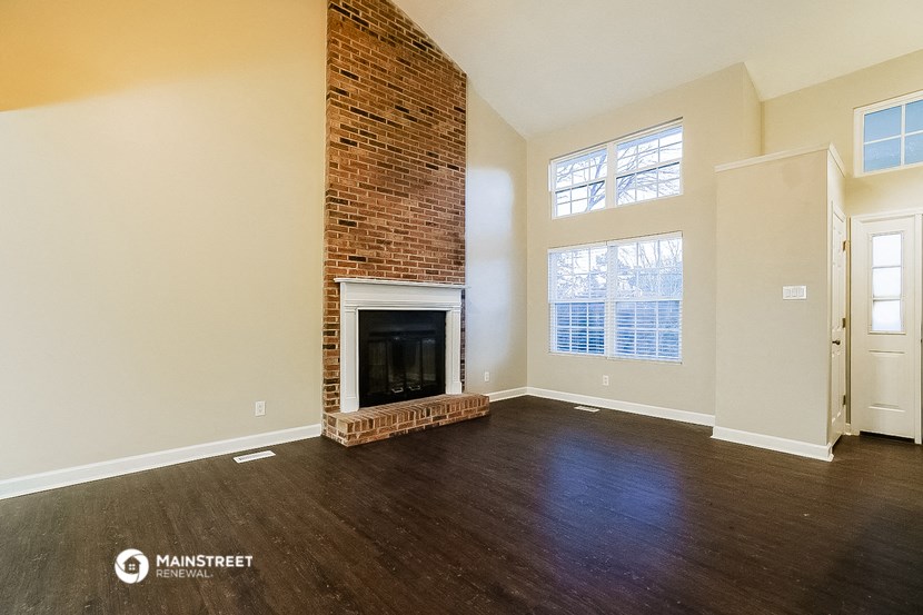 an empty living room with a brick fireplace and wooden floors