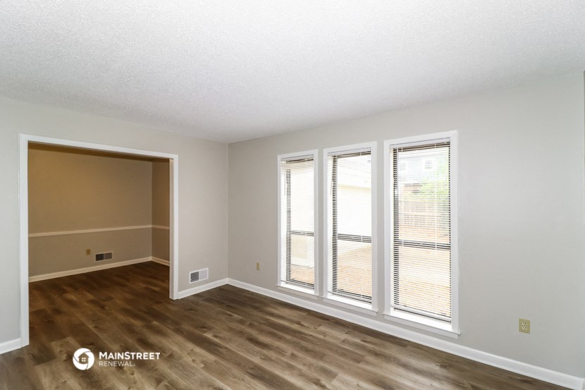 the living room of an apartment with wood flooring and large windows