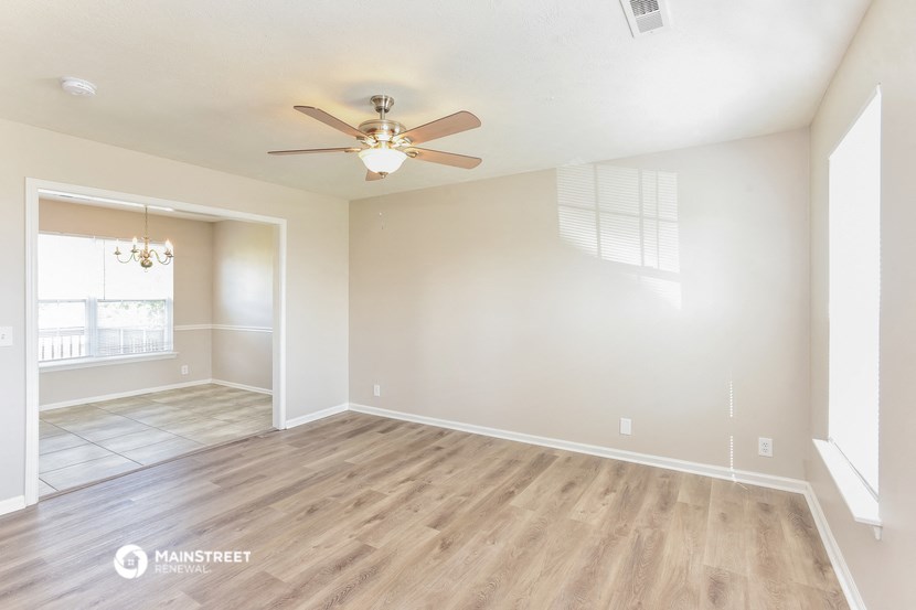 the spacious living room with wood flooring and a ceiling fan
