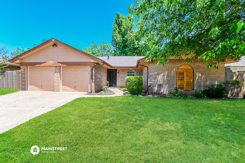 a tan brick house with a driveway and a lawn