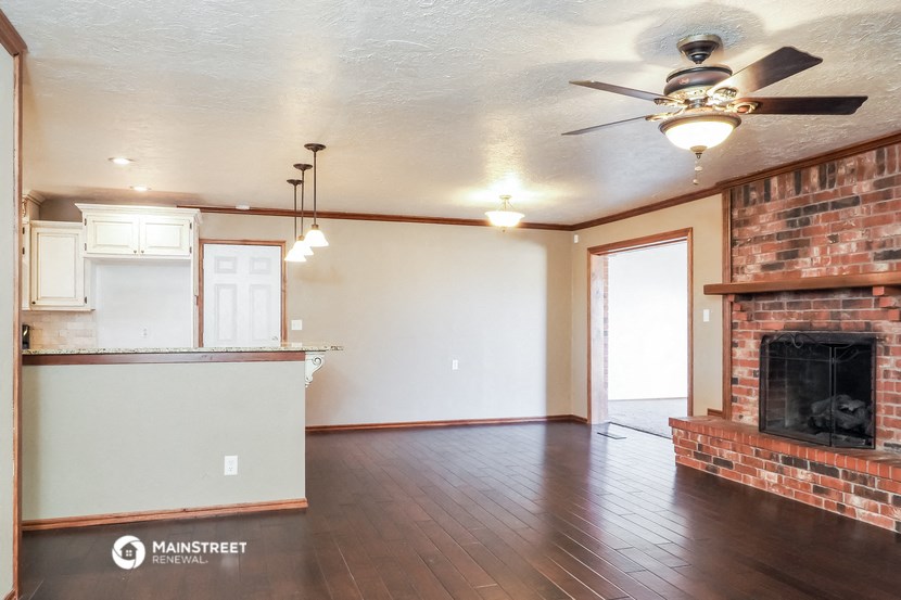 an empty living room with a brick fireplace and a ceiling fan