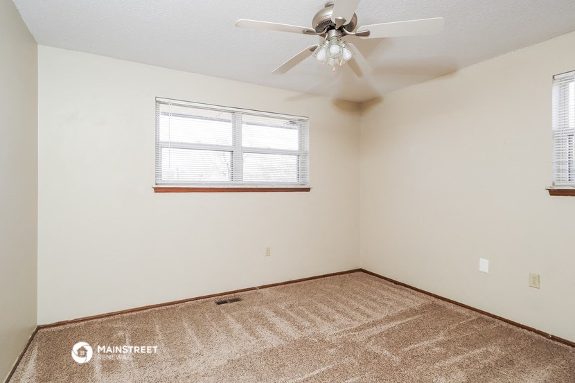 the living room of an empty room with a ceiling fan and a window