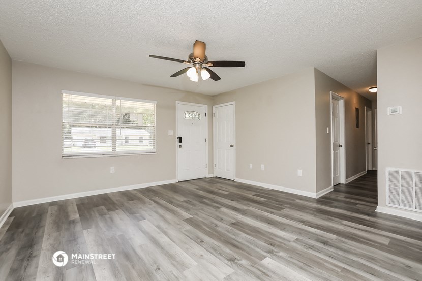 an empty living room with a ceiling fan and a door to a hallway