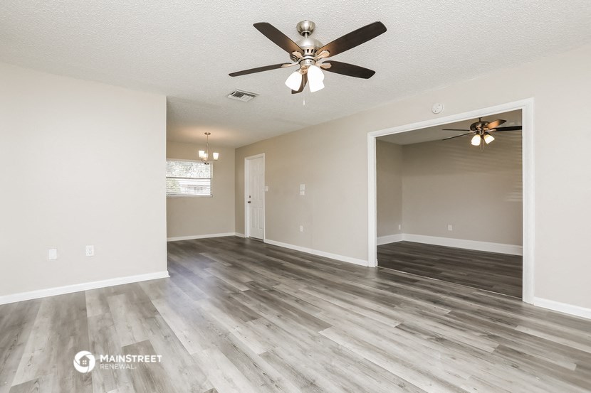 the spacious living room with a ceiling fan and a door to the bathroom