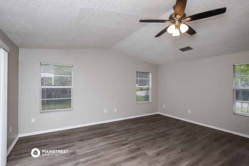 the spacious living room of an empty home with a ceiling fan