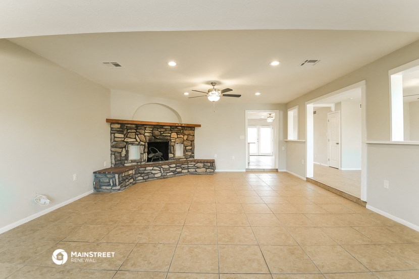 an empty living room with a stone fireplace and tile flooring