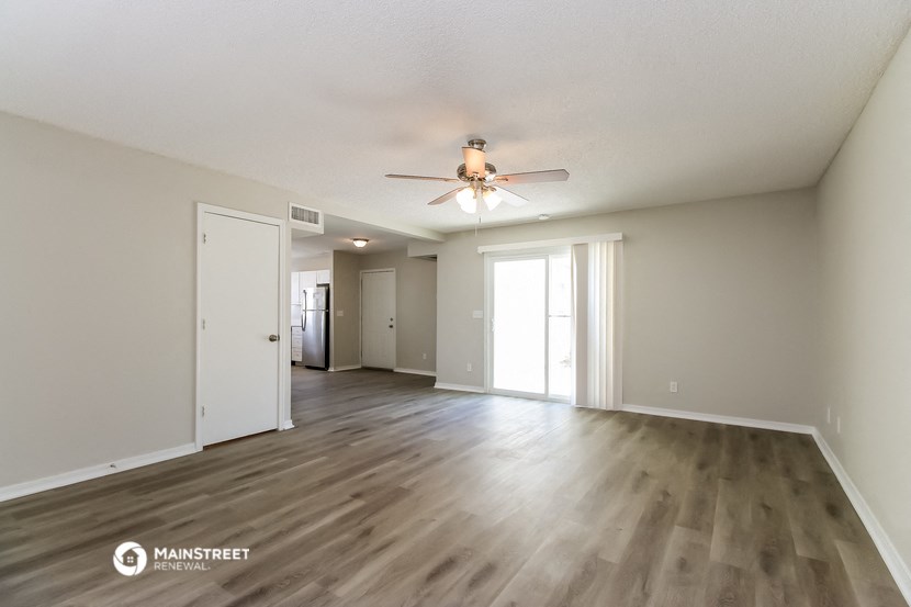 the living room and dining room of an apartment with wood floors and a ceiling fan