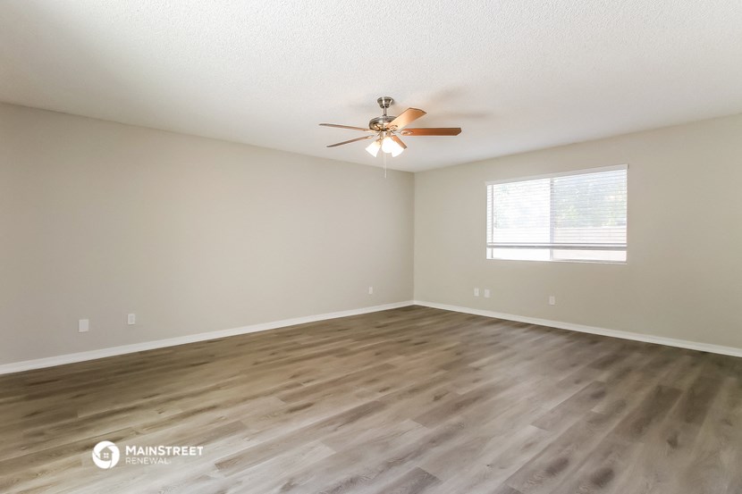 the spacious living room with hardwood floors and a ceiling fan