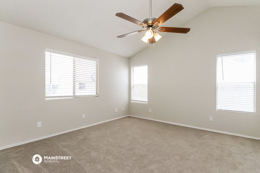 the spacious living room with ceiling fan and windows