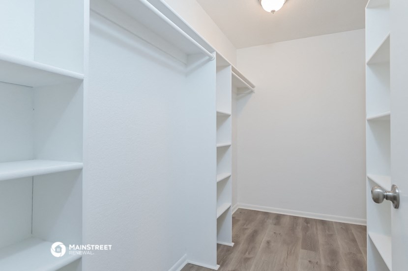 a walk in closet in a white room with shelves and a door