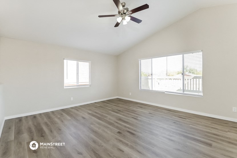 the spacious living room with wood flooring and a ceiling fan