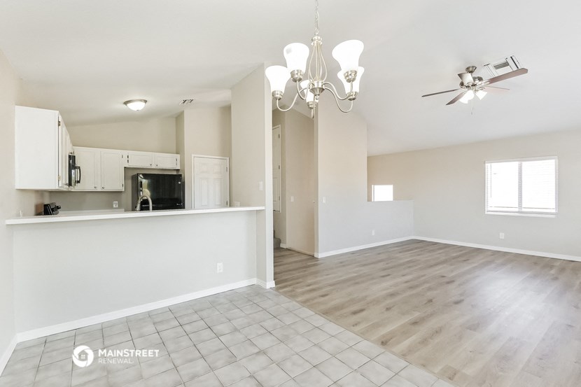 an empty living room with a kitchen and a chandelier