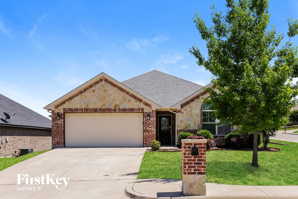 A house with a garage door and a brick pillar in front of it.