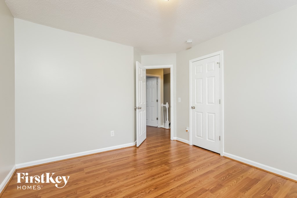 a bedroom with white walls and wood floors and a door to a hallway
