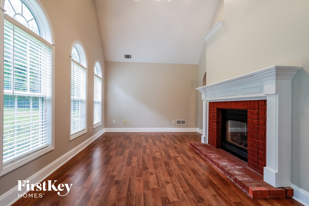 an empty living room with a brick fireplace and wooden floors