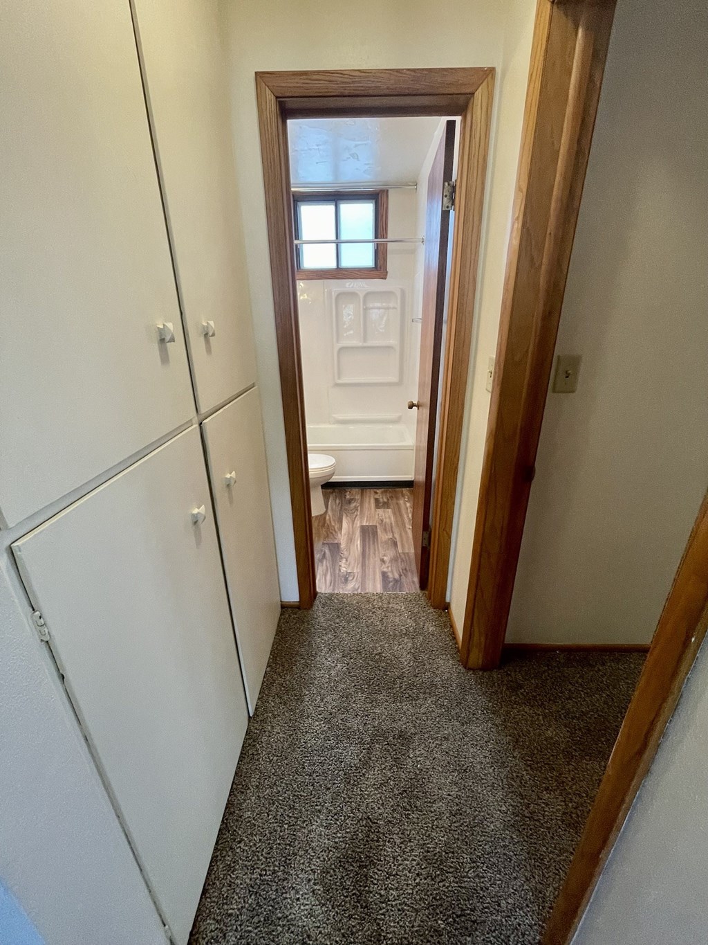 a look down the hallway of a bathroom with white cabinets and a toilet