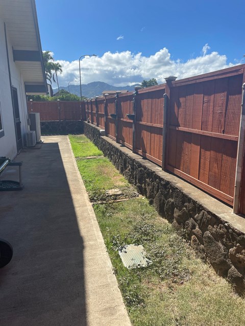 A brown fence runs along a grassy area next to a building.