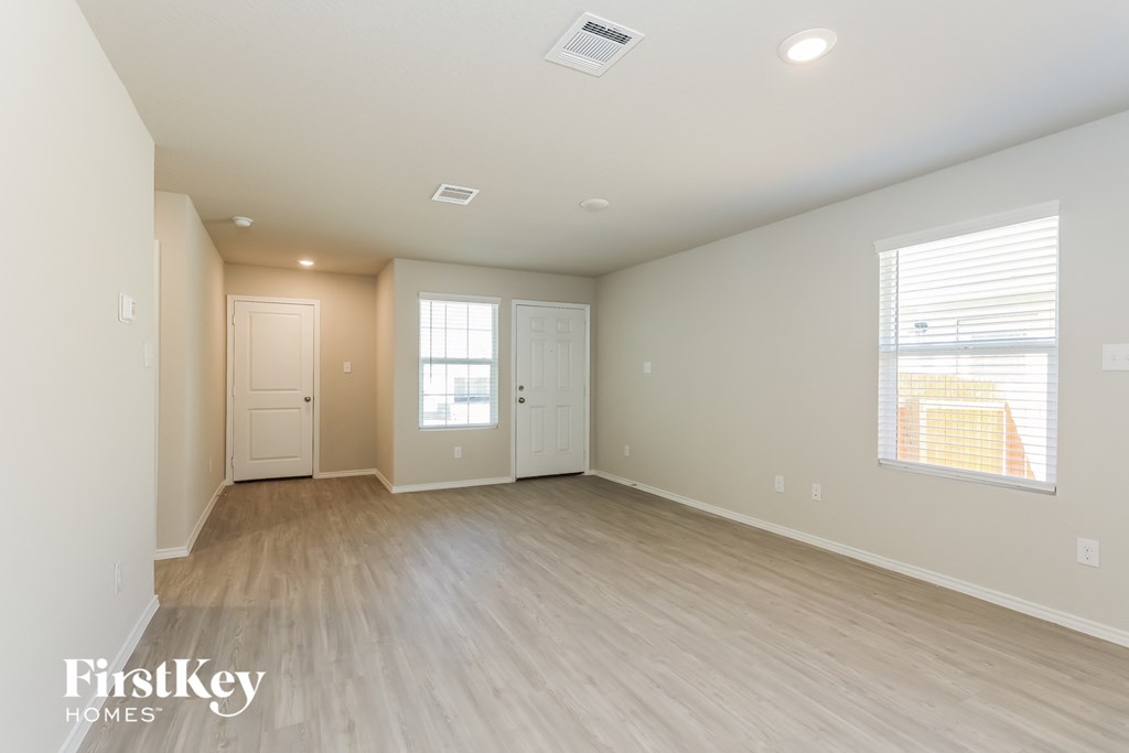 A spacious empty room with light wood flooring and white walls.
