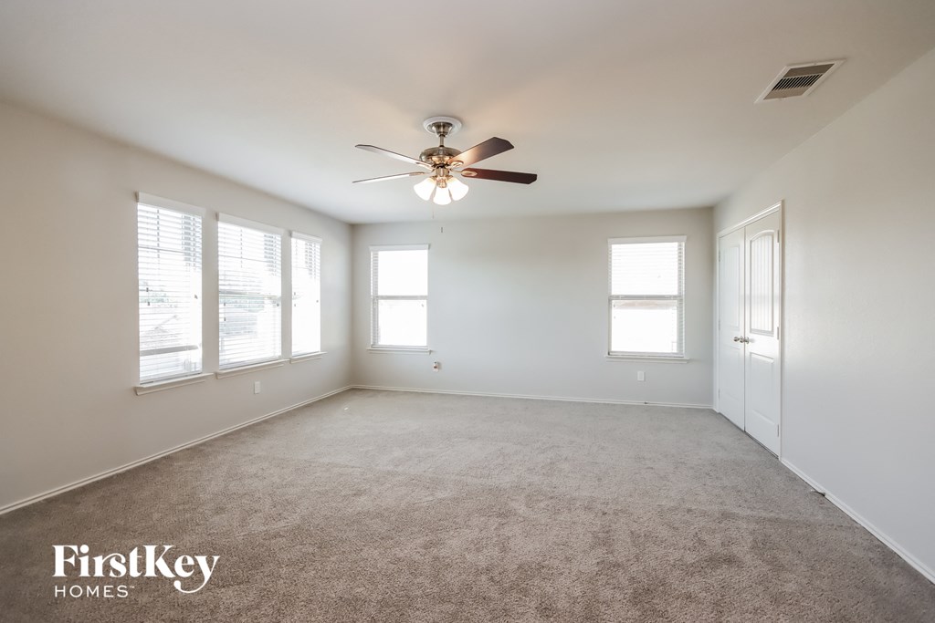 an empty living room with a ceiling fan and windows