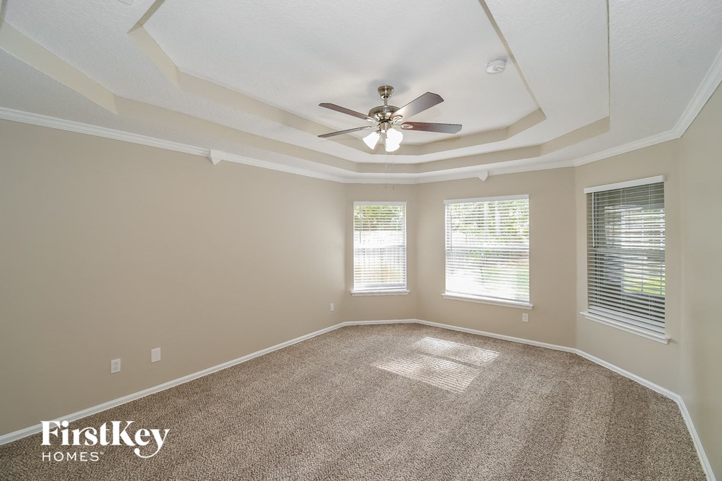 an empty living room with a ceiling fan and three windows