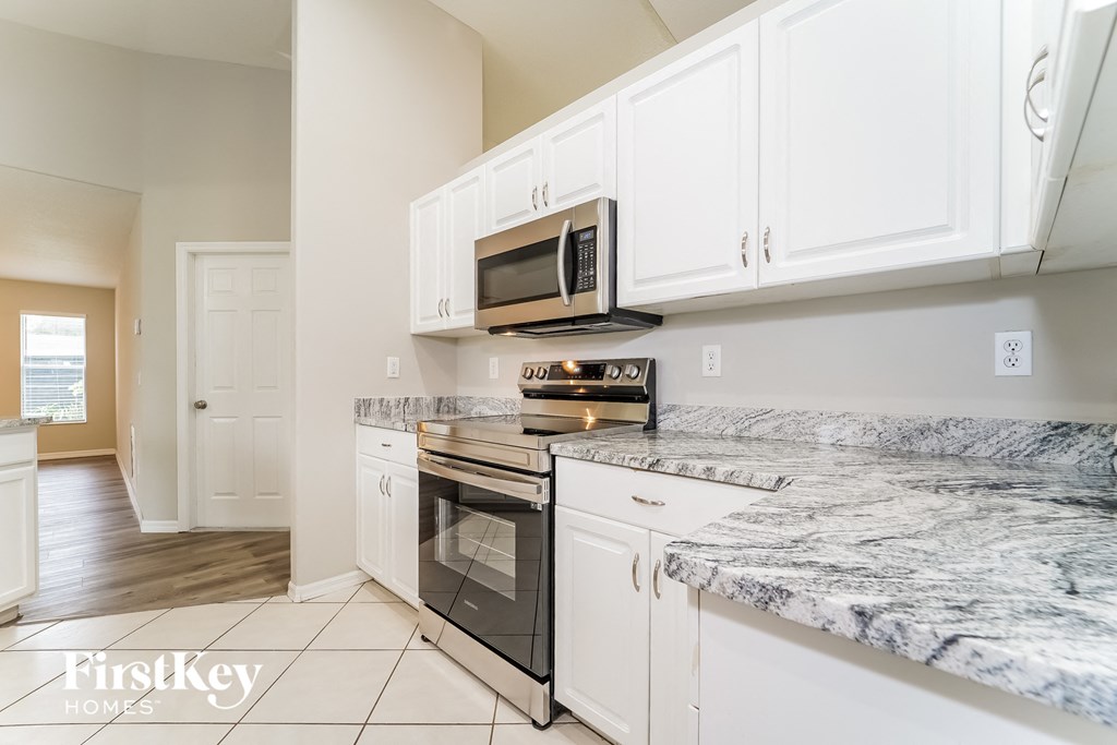 a kitchen with white cabinets and marble counter tops and a stove and microwave