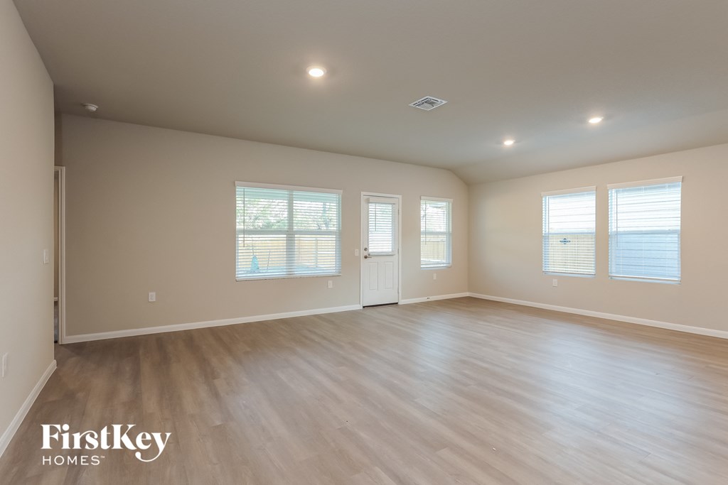 A spacious room with wooden flooring and three windows.
