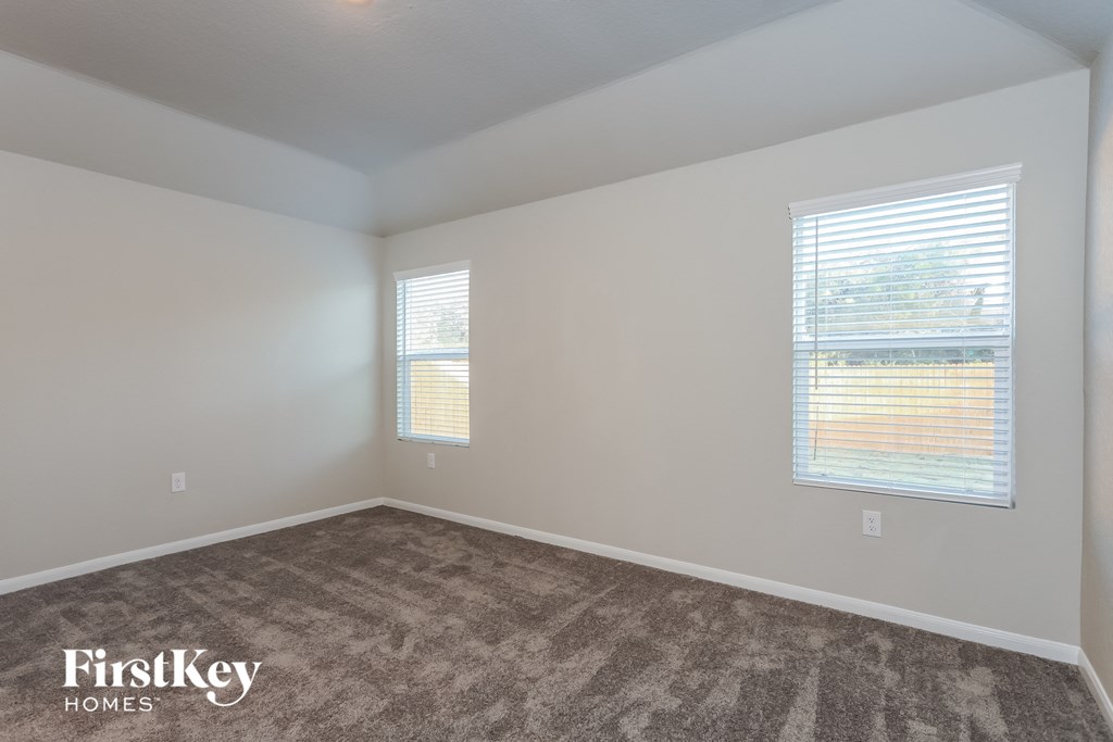 A room with a carpeted floor and two windows with blinds.