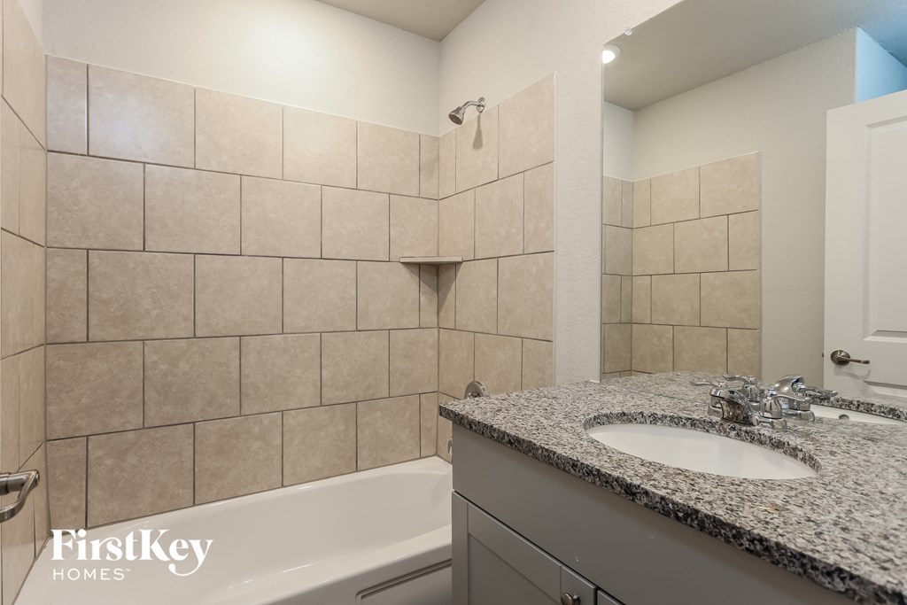 A bathroom with a tub, sink and tiled walls.