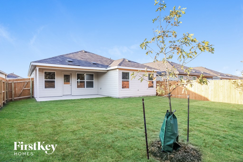 A white house with a brown roof and a green tree sapling in the front yard.