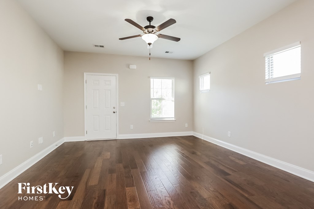 the spacious living room with hardwood flooring and a ceiling fan