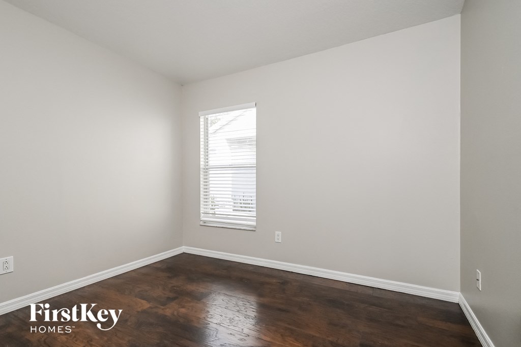a bedroom with white walls and wood floors and a window
