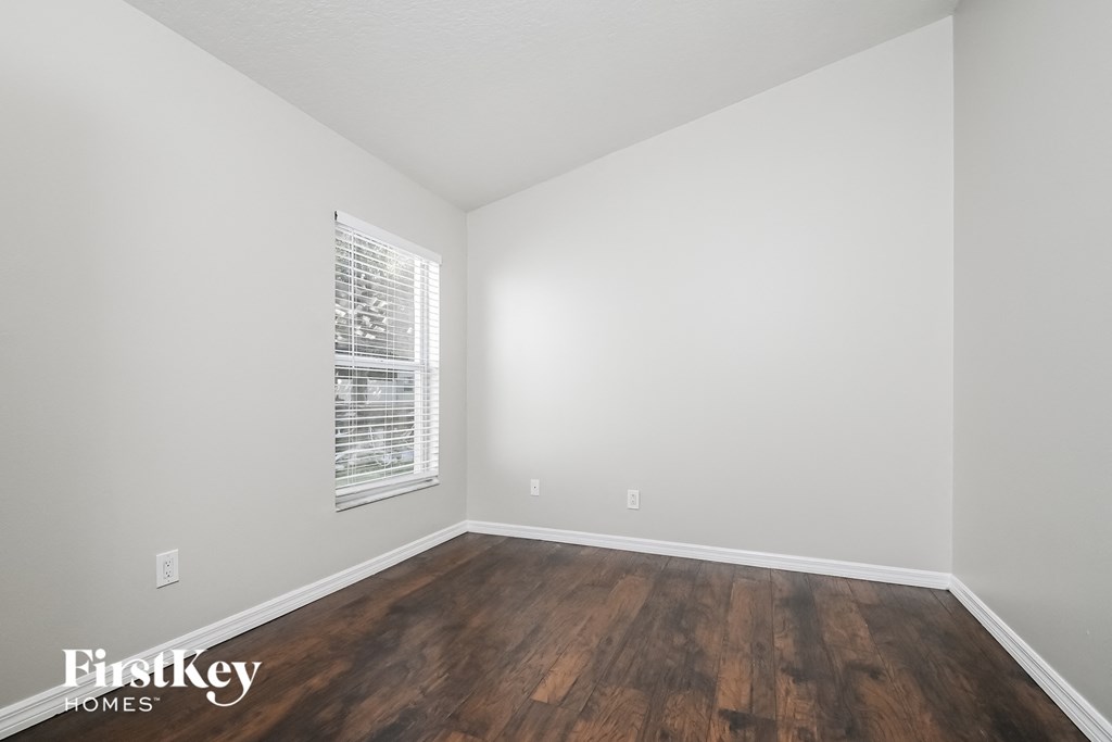 a bedroom with white walls and wood flooring and a window