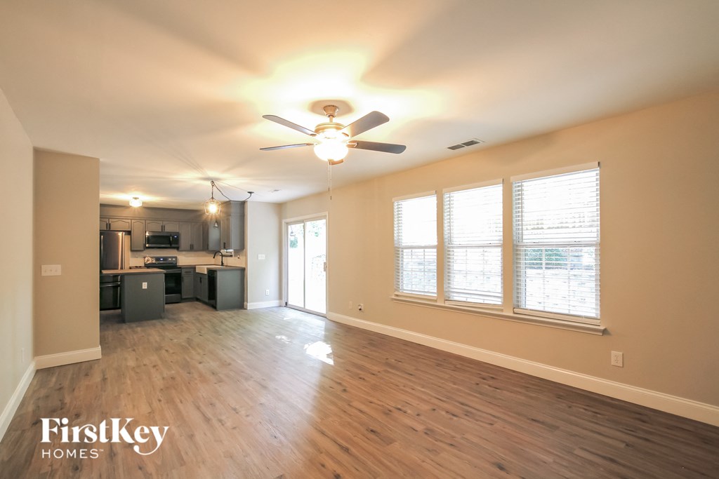 an empty living room with a ceiling fan and a kitchen