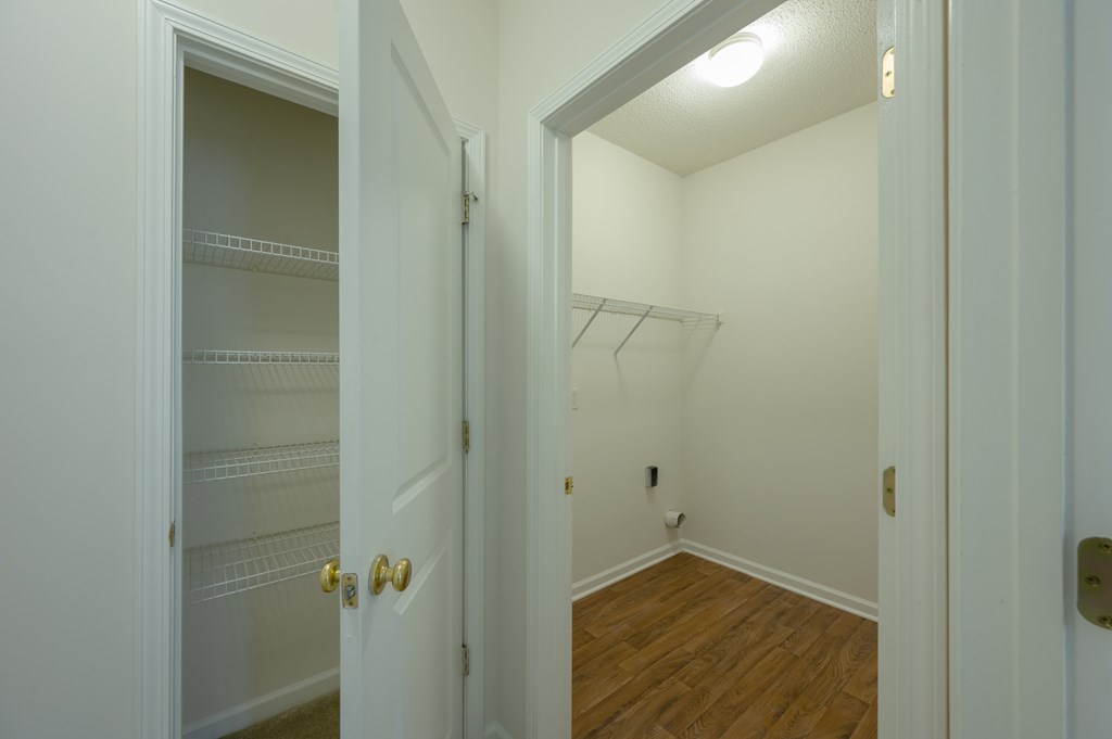 A white door with a gold handle is open to a room with a white wall and a wooden floor.