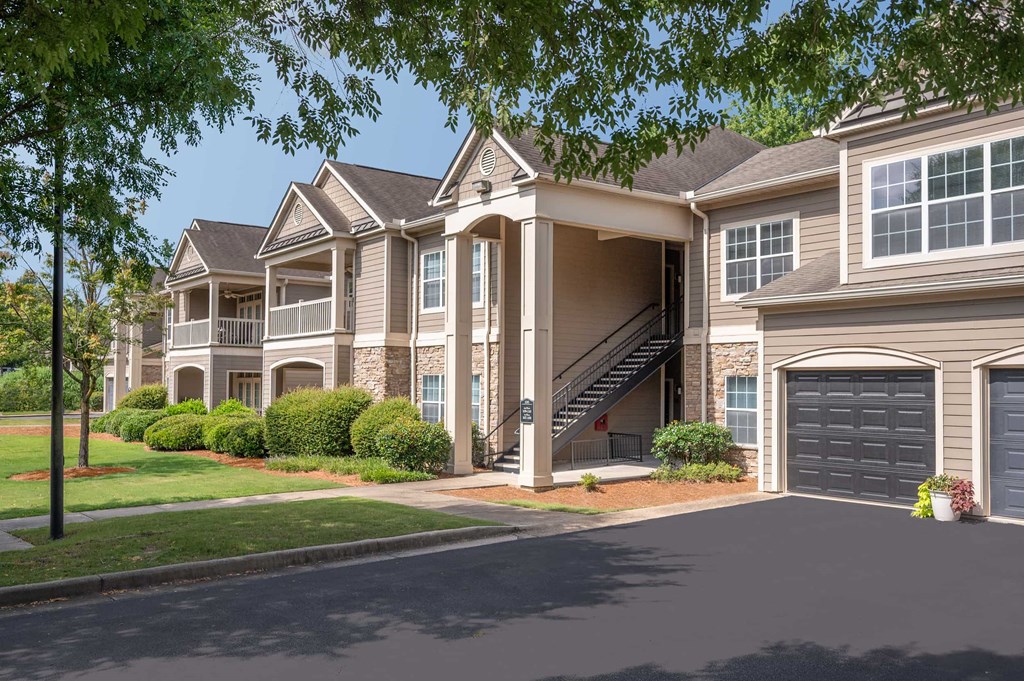 A large, two-story house with a garage is surrounded by a well-manicured lawn and trees.