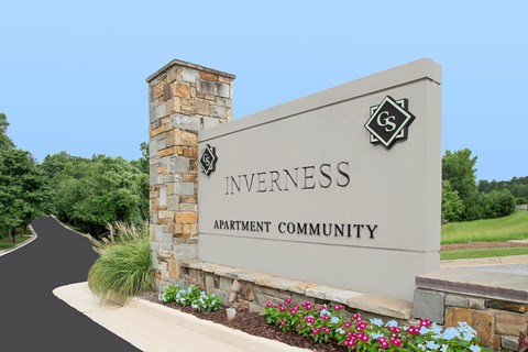 A sign for Inverness Apartment Community with a stone pillar and flowers in front.