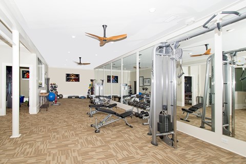 A gym with a mirrored wall and a ceiling fan.