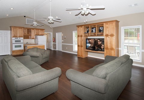 Two grey couches in a living room with a television and a kitchen in the background.